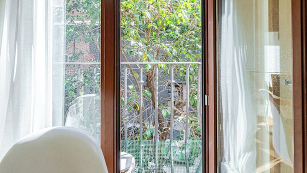 Ein Zimmer mit Tisch, Stuhl und einem Balkon mit Blick auf Bäume und einen Zaun.