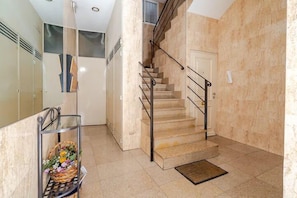 Una escalera con barandilla de metal que lleva a una puerta, una alfombra pequeña al pie y una vitrina de vidrio con flores a la izquierda.
