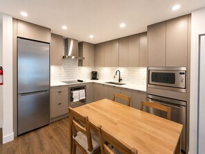 A modern kitchen with a stainless steel refrigerator, built-in oven, microwave, and a wooden dining table with chairs.