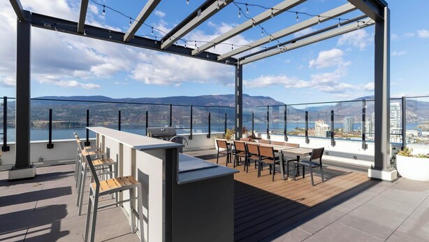 A rooftop terrace with a bar area, seating, and a view of the city and mountains.