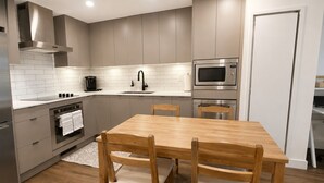 A modern kitchen with a wooden dining table and chairs, a built-in oven, a microwave, and a stainless steel range hood.