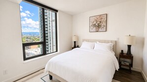 Une chambre avec une grande fenêtre, un lit, deux tables de chevet avec des lampes et un tableau au mur.