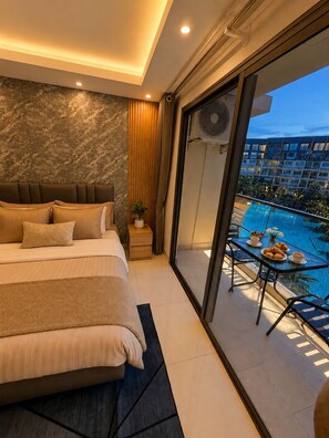 A bedroom with a large bed, a view of a swimming pool, and a balcony with outdoor seating. - Laguna beach resort 2 Jomtien beach condominium - Apartment free electricity (Muang Pattaya)