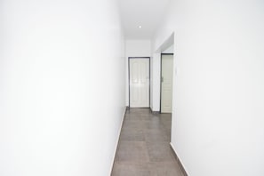A hallway with a white door at the end, a tiled floor, and white walls. - Land Of Grace Panyumba (Victoria Falls)