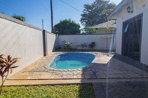 A swimming pool with a tiled deck, surrounded by a low wall and a small garden area. - Land Of Grace Panyumba (Victoria Falls)