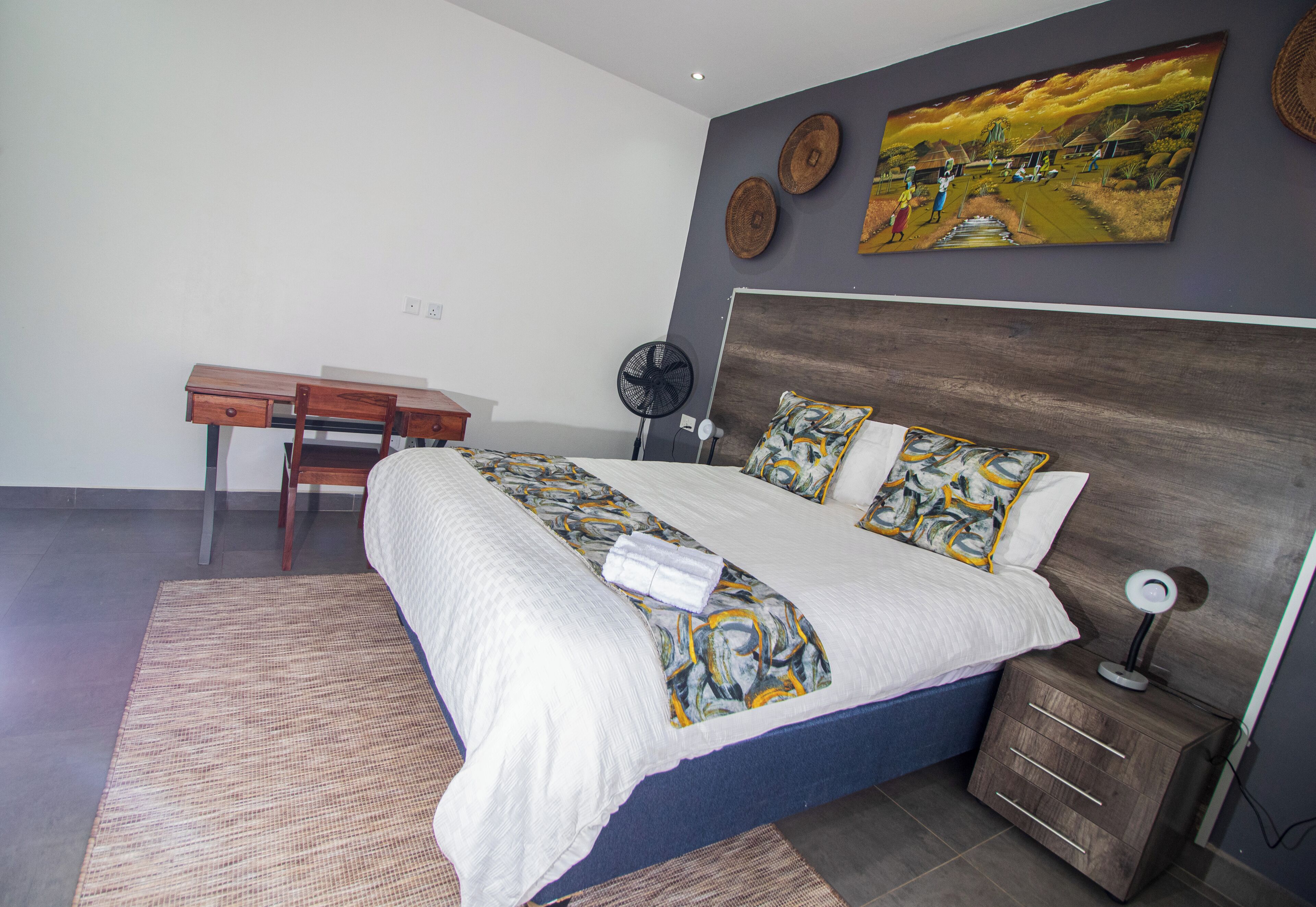 A bedroom with a bed, bedside table, lamp, and a desk with chair.