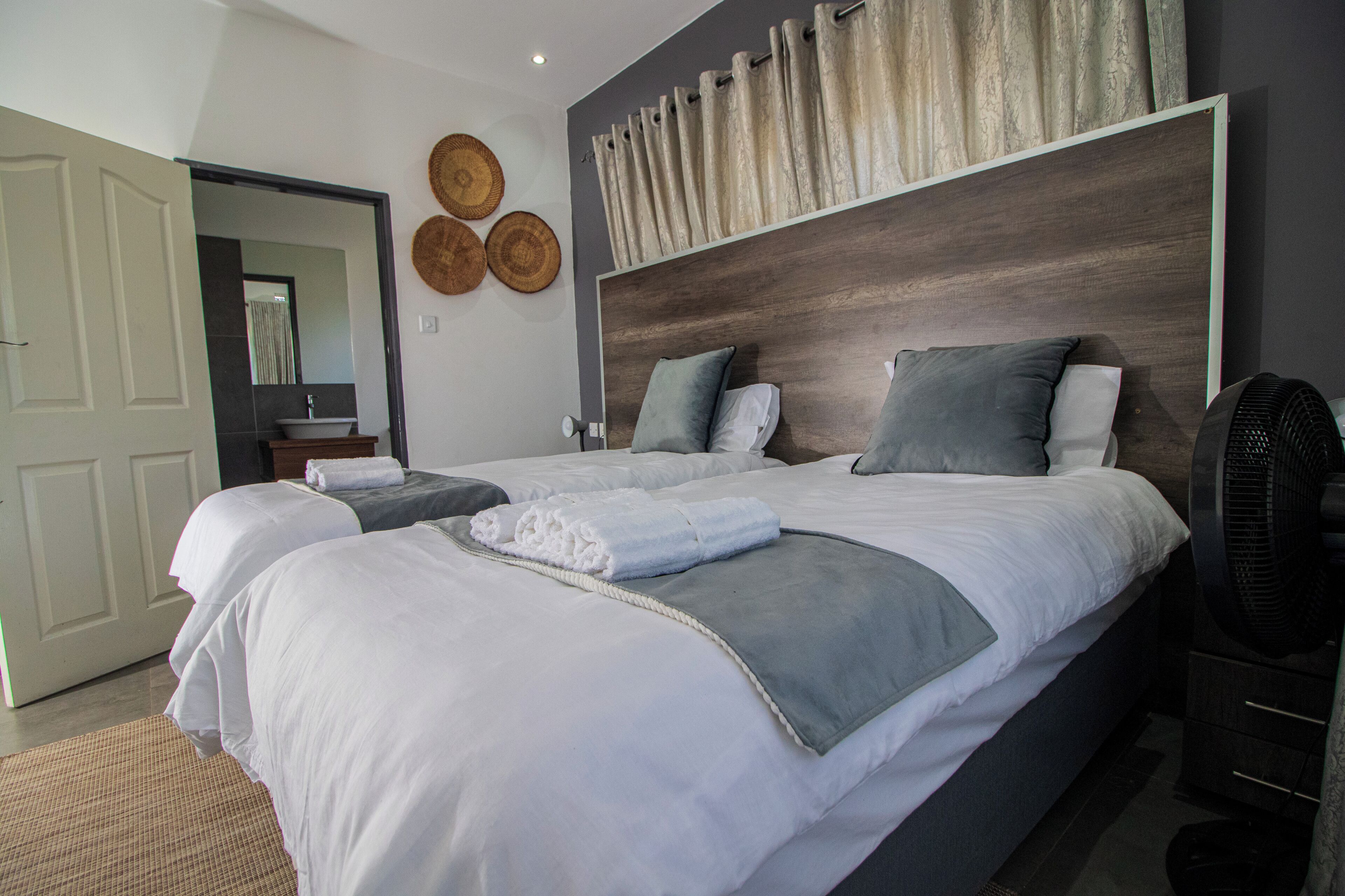 A modern bedroom with a large bed, bedside tables, a mirror, and a fan.