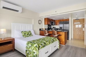 Ein Hotelzimmer mit Bett, Nachttisch, Lampe und einer Küchenzeile, inklusive Kühlschrank, Mikrowelle und Spüle.