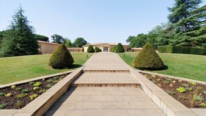 A pathway leading to a building with a tiled roof, surrounded by well-maintained hedges and trees.