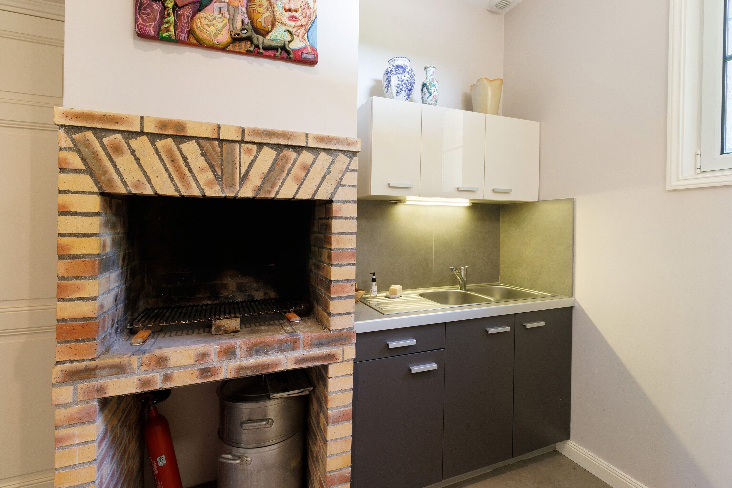 Una cocina con horno de ladrillo, un lavabo, armarios y un elemento decorativo en la pared.