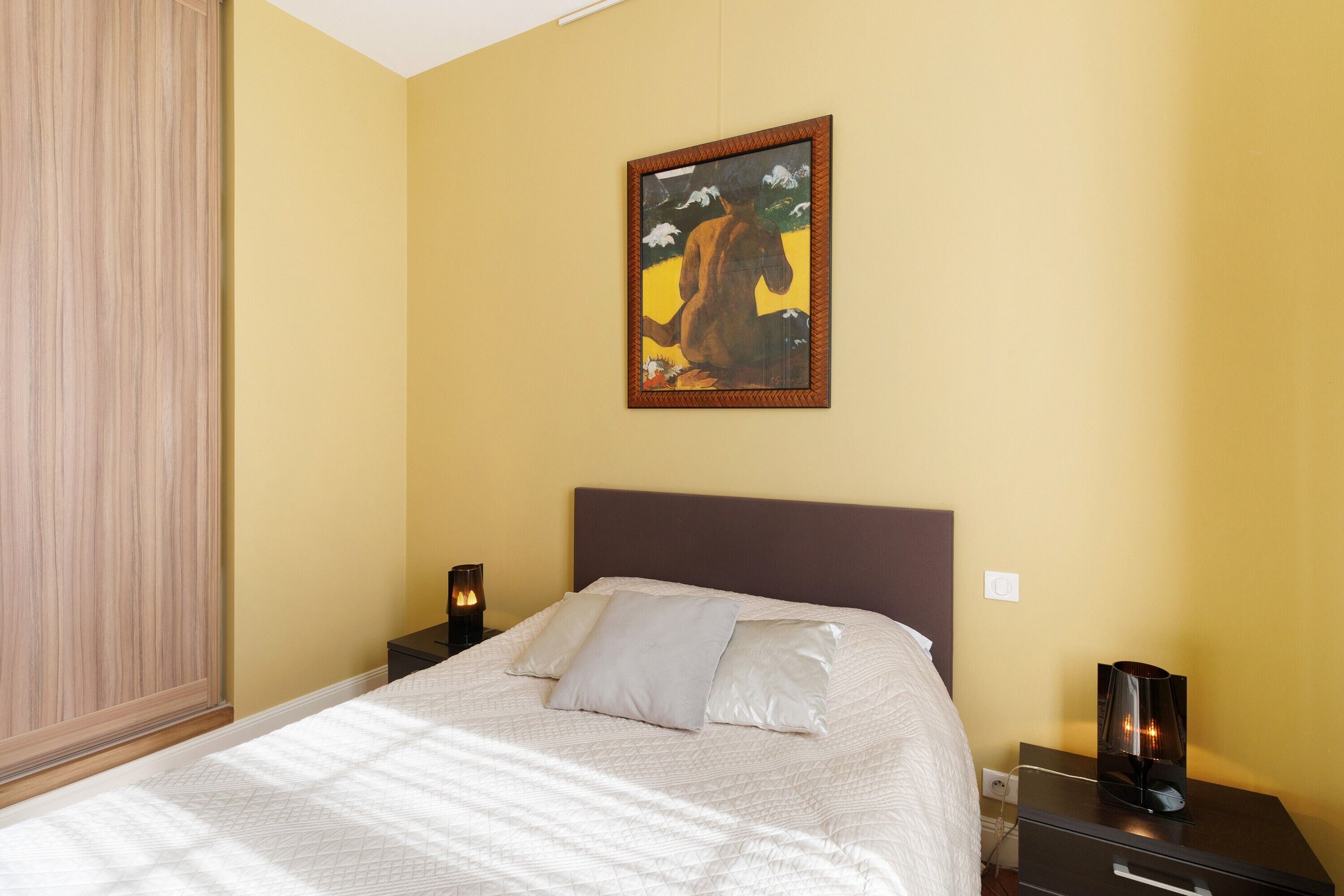Ein Schlafzimmer mit einem Bett, einem Nachttisch, einer Lampe und einem Bild an der Wand.
