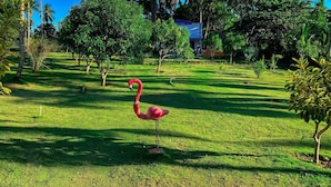 Un espacio cubierto de césped con una estatua de flamenco, rodeado de árboles y un edificio al fondo.