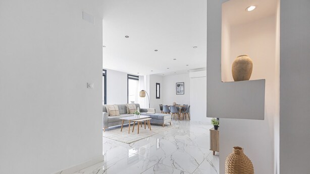 A modern living room with a marble floor, a sofa, a coffee table, and a dining area with chairs and a table.
