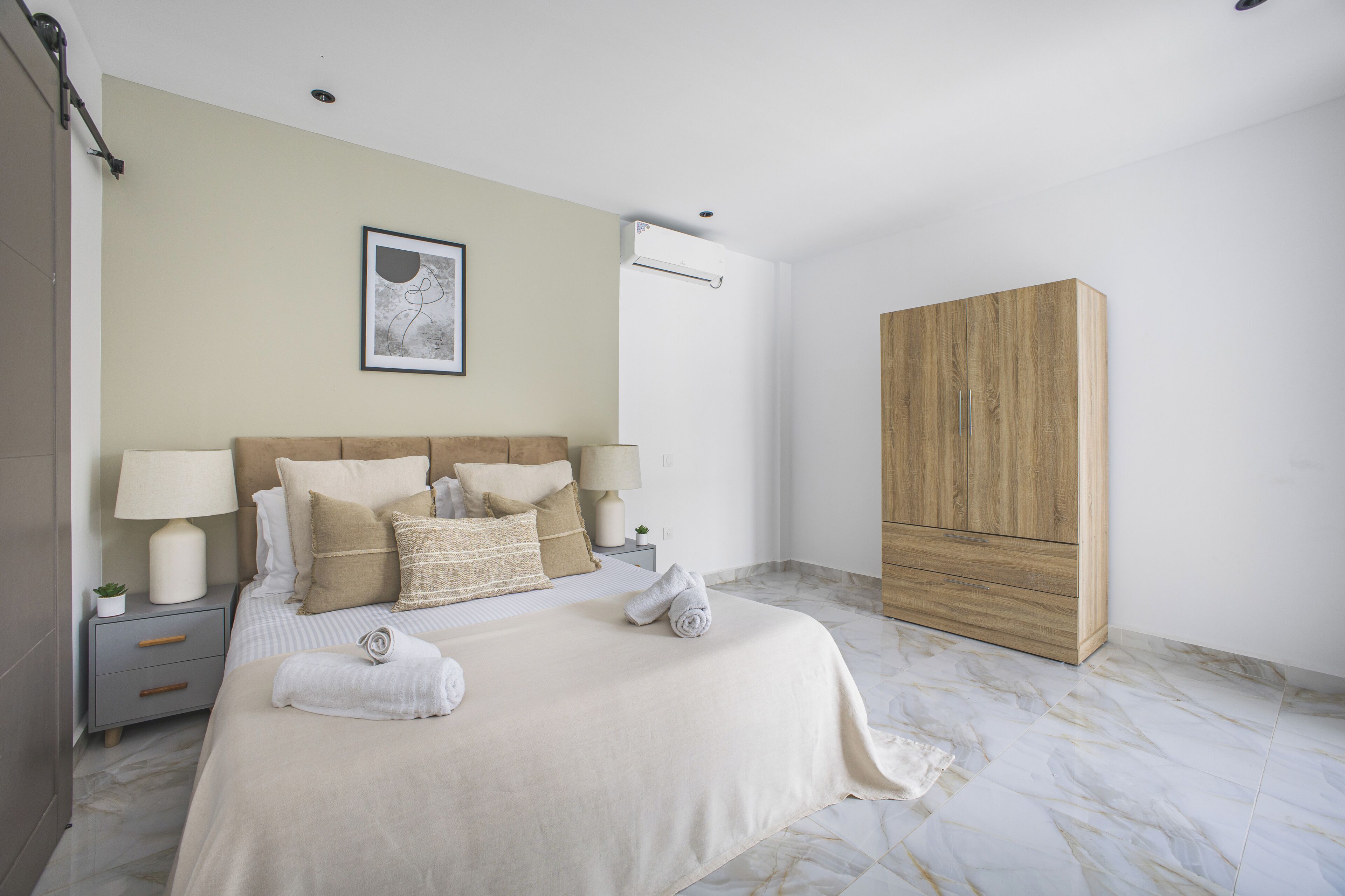 Un dormitorio con cama, lámparas de noche, un armario y un cuadro en la pared.