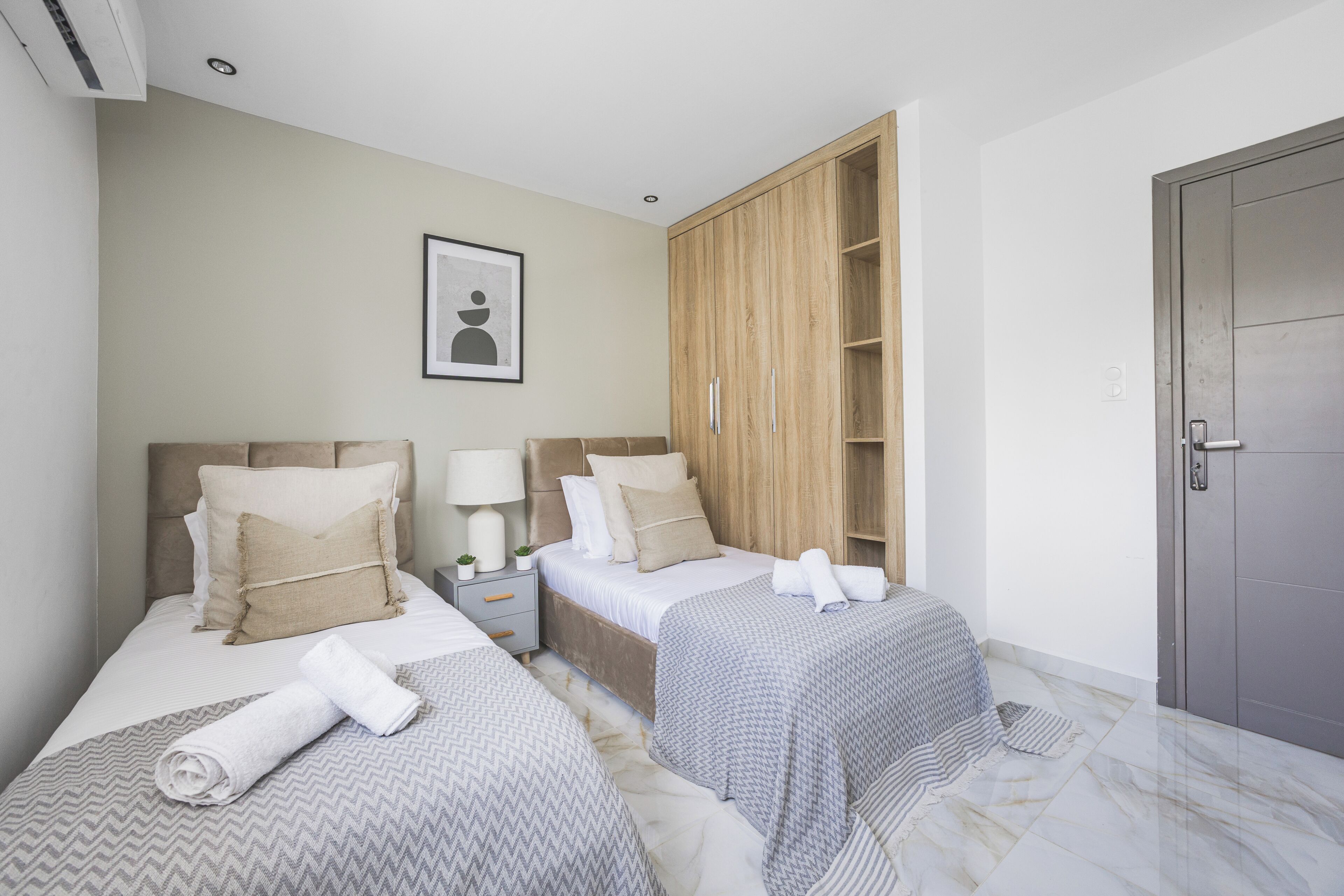 Une chambre d’hôtel avec deux lits, une armoire, une table de chevet avec une lampe et une porte.