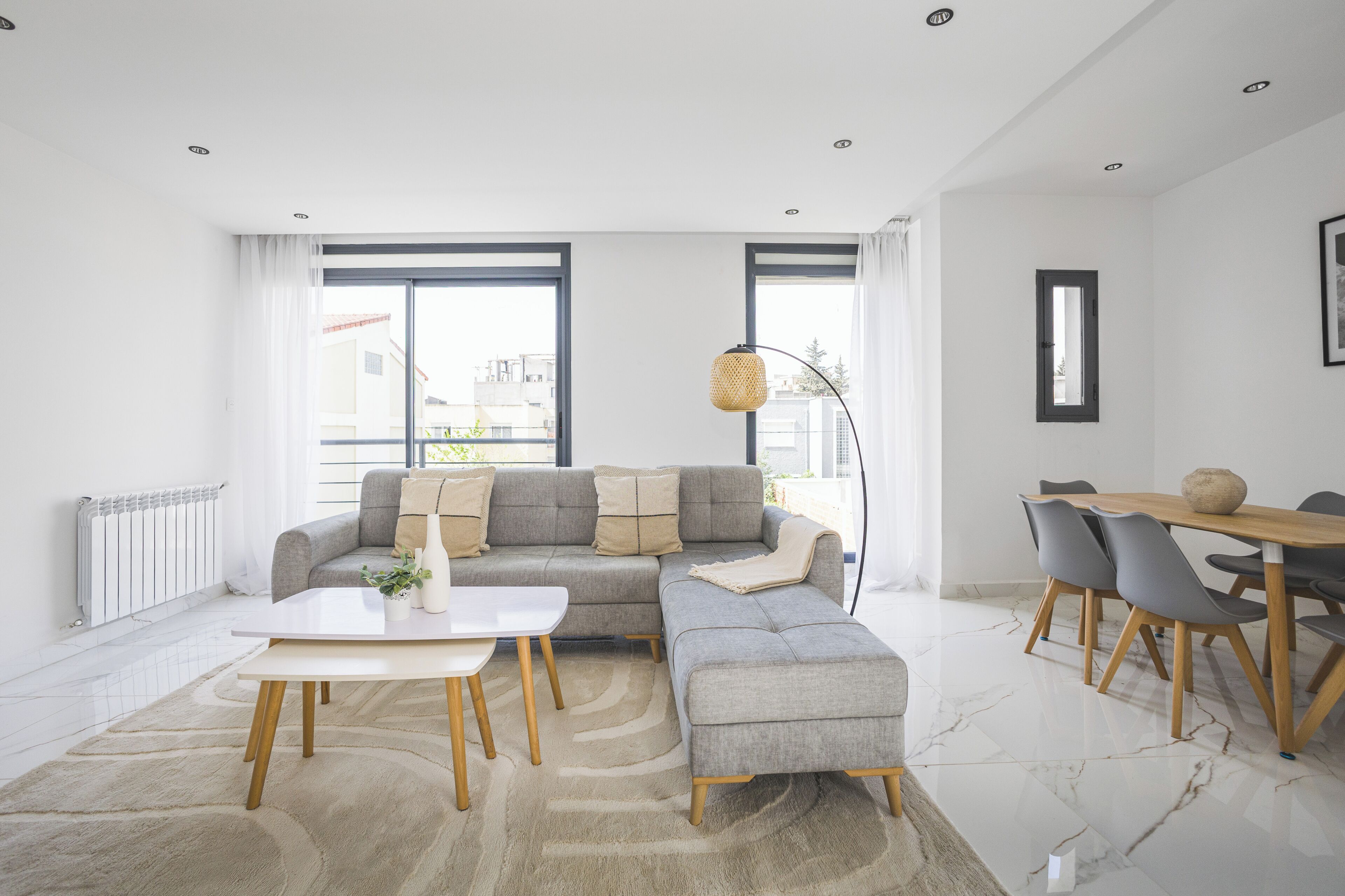 A modern living room with a sectional sofa, a dining table with chairs, and a large window providing natural light.