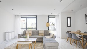 A modern living room with a sectional sofa, a dining table with chairs, and a large window providing natural light.