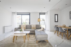 Una sala de estar moderna con un sofá modular, una mesa de comedor con sillas y un ventanal que proporciona luz natural.