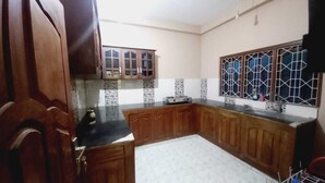 A kitchen with wooden cabinets, a black countertop, and a window with a geometric pattern. - Kamaleswari Villa Trincomalee | 3BR House | 2km to Beach | Family Stay (Trincomalee)