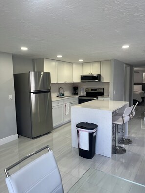 A modern kitchen with stainless steel appliances, a central island, and bar stools. - 2-bedroom house in pleasant Port Richey with cool AC (Port Richey)