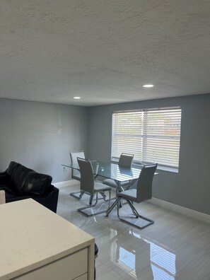 A modern meeting room with a glass table, metal chairs, a white desk, and a window with blinds. - 2-bedroom house in pleasant Port Richey with cool AC (Port Richey)