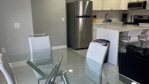 Una cocina moderna con un refrigerador de acero inoxidable, armarios blancos y una mesa de vidrio con sillas.