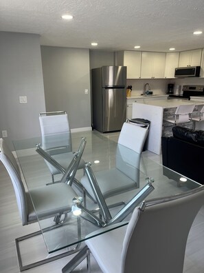 A modern kitchen with a stainless steel refrigerator, white cabinets, and a glass dining table with chairs. - 2-bedroom house in pleasant Port Richey with cool AC (Port Richey)