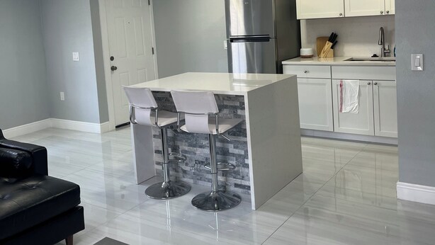Una cocina moderna con armarios blancos, un refrigerador de acero inoxidable y una barra con taburetes.