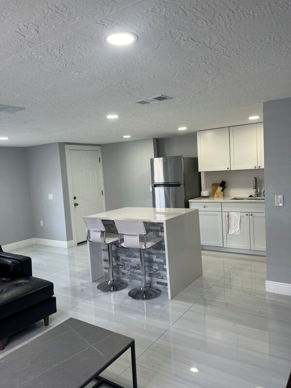 A modern kitchen with white cabinets, a stainless steel refrigerator, and a bar area with stools. - 2-bedroom house in pleasant Port Richey with cool AC (Port Richey)