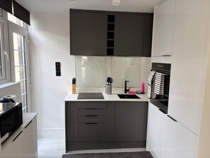 A modern kitchen with a white countertop, dark cabinets, a built-in oven, and a window with blinds. - Stylish 2Bed Flat-Fast WiFi-Close to Shops, Restaurants & Train Station-Sleeps 5 (Croydon)