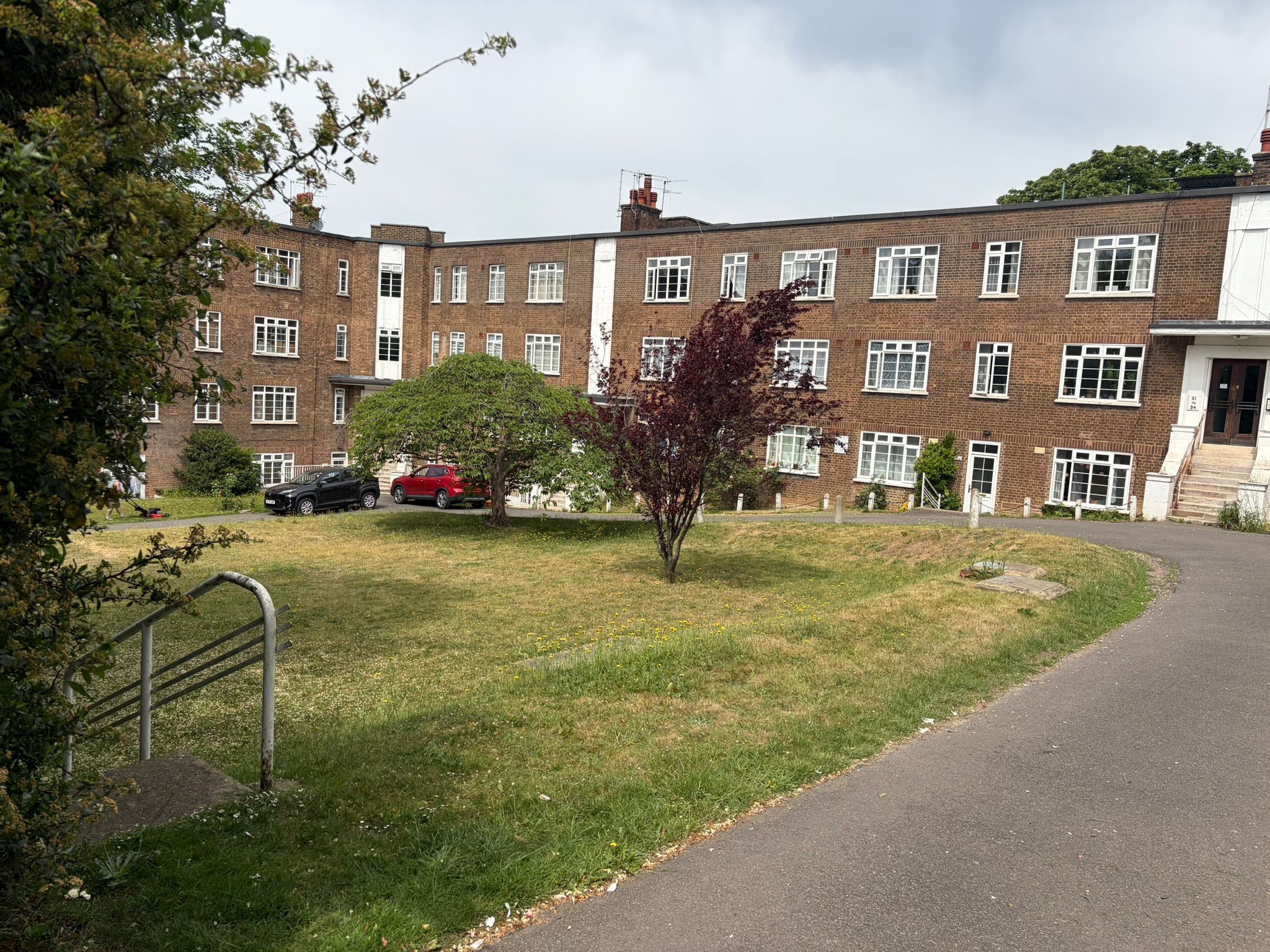 A multi-story brick building with a central lawn, a staircase, and a pathway leading to the entrance.