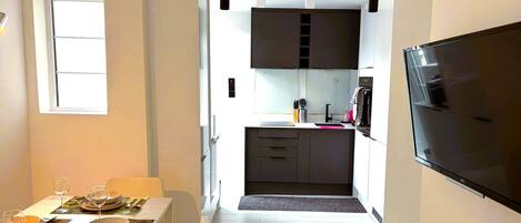 Una cocina moderna con televisor, comedor con mesa lista para usar y una ventana.