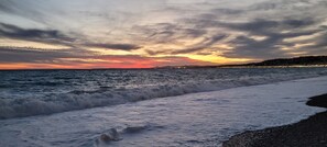 A beach with waves, a sunset, and a distant cityscape. - Air-conditioned apartment in the heart of town, just 7' from the beach! (Nice)