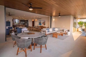 A spacious living area with a round table and chairs, a sofa, and a kitchen in the background. - Tau - Condo Kumar Inside the Gates (Punta Mita)