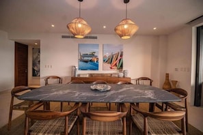 A dining area with a marble table, wicker chairs, and two hanging light fixtures. - Tau - Condo Kumar Inside the Gates (Punta Mita)
