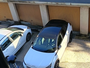 Dos coches aparcados, uno blanco y otro negro, frente a un edificio con una puerta marrón y una pared de hormigón.