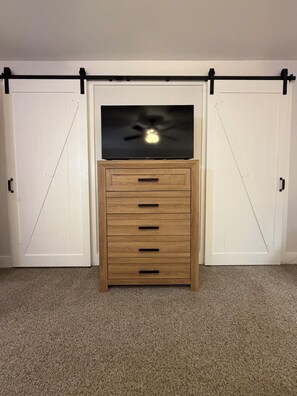 A room with a TV on a wooden cabinet, two white doors, and a carpeted floor. - Cozy High Point Stay (High Point)