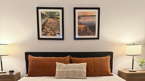 Ein ordentlich bezogenes Bett mit einer braunen Decke, zwei Kissen und zwei gerahmten Bildern an der Wand darüber.