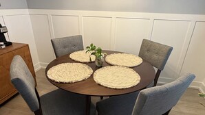 Ein runder Esstisch mit gewebten Tischsets, grau gepolsterten Stühlen und einer Kaffeemaschine auf einem Holztisch.