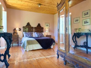Ein Schlafzimmer mit Holzboden, Holzzieldecke, einem Bett mit dunklem Kopfteil und einem großen Spiegel.