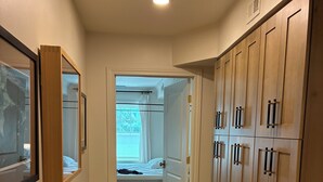 Ein Flur mit Holzboden, einem Bett mit weißem Kopfteil und einem Wandschrank mit mehreren Türen.