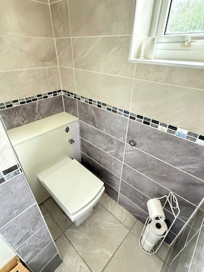 A bathroom with a toilet, a shower area, and a window. - 3 Bed House Contractor Friendly Long Stays Welcome (Bedford)