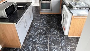 A compact kitchen with a gas stove, oven, microwave, and a washing machine. - 3 Bed House Contractor Friendly Long Stays Welcome (Bedford)