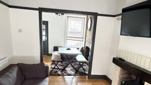 A living room with a sofa, a coffee table, a fireplace, a dining area with a table and chairs, and a TV mounted on the wall. - 3 Bed House Contractor Friendly Long Stays Welcome (Bedford)