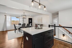 A modern kitchen with a central island, dining area with chairs, and a staircase. - Fire Pit, BBQ & Room for Everyone, Spacious 4BR/3BA in Hendersonville (Hendersonville)
