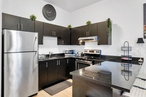 Una cocina moderna con electrodomésticos de acero inoxidable, armarios oscuros y una isla central.