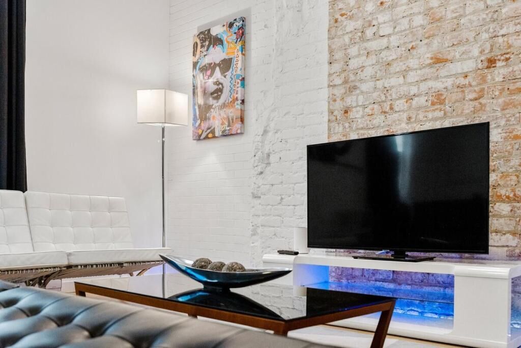 A modern living room with a white brick wall, a flat-screen TV, a white sofa, a coffee table, and a floor lamp.