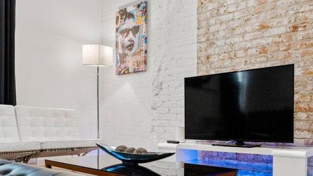 Ein modernes Wohnzimmer mit weißer Backsteinwand, Flachbildfernseher, weißes Sofa, Couchtisch und Stehlampe.