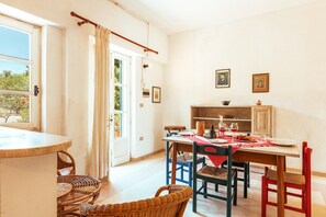 A dining area with a table set for two, wicker chairs, a wooden cabinet, and a window with curtains. - Nona Dimora Del Pizzo - Gallipoli (Gallipoli)