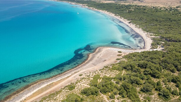 Vista aérea de uma área costeira com águas turquesa cristalinas, uma praia de areia e vegetação verde exuberante.